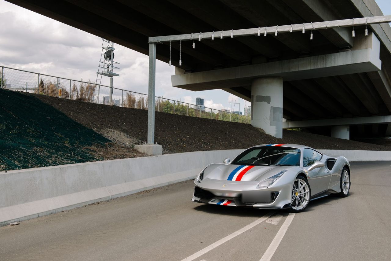 Silver Ferrari 488 Pista with a blue, white and red stripe, parked under a freeway overpass