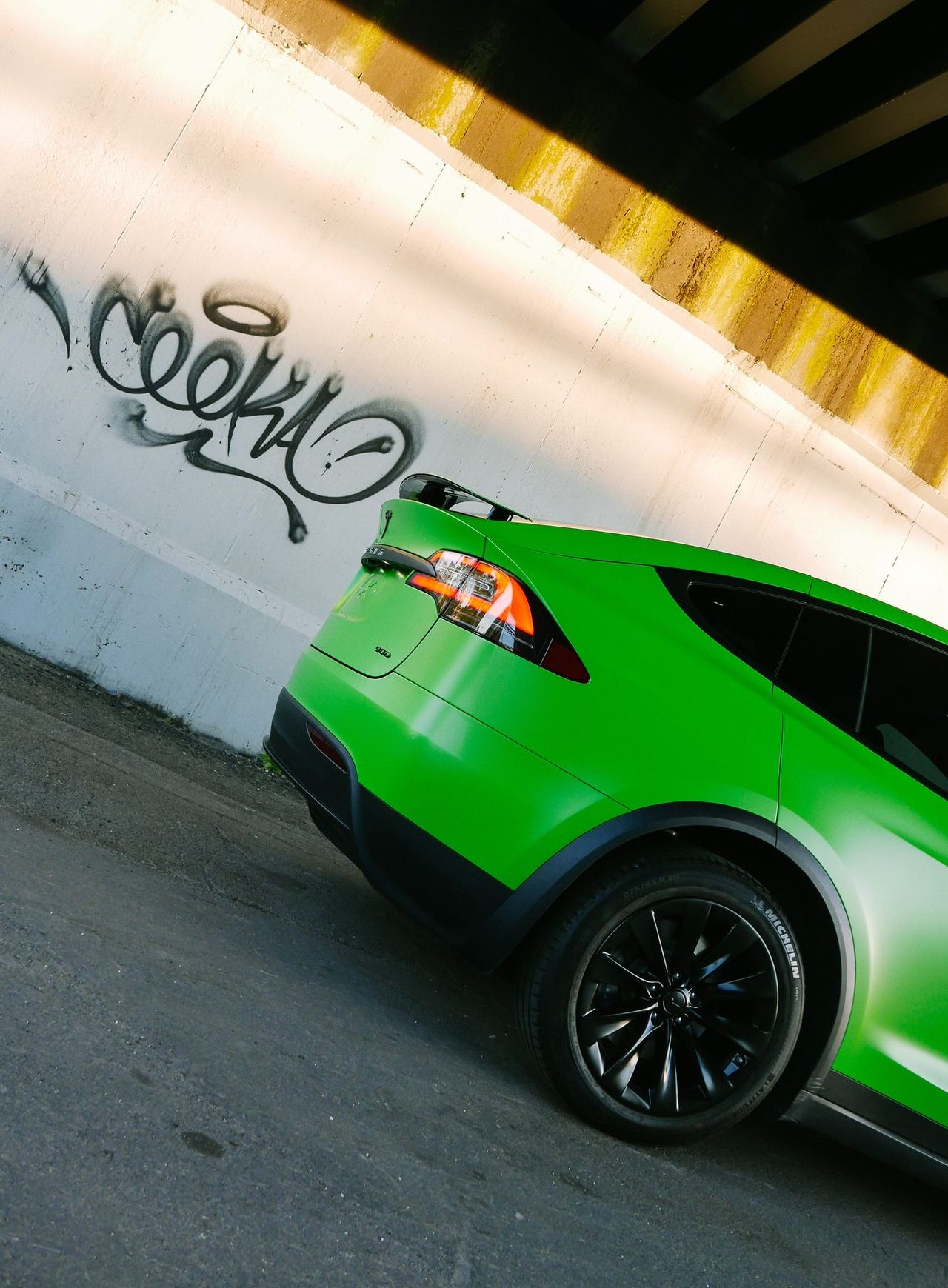 Tesla Model X wrapped in bright green, rear three-quarter view beside a graffiti wall